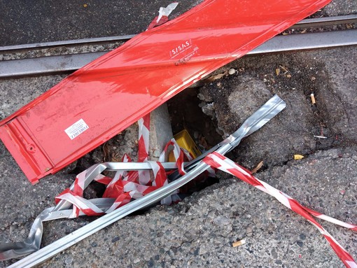 Buco nella strada con binario a poca distanza e transenna