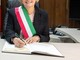 Donna sindaco con fascia tricolore che firma documenti