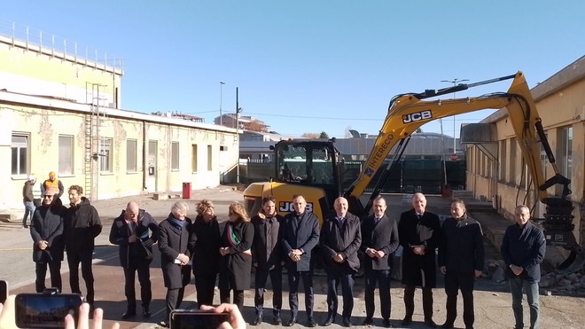 persone schierate di fronte a una benna meccanica