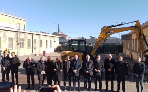 persone schierate di fronte a una benna meccanica