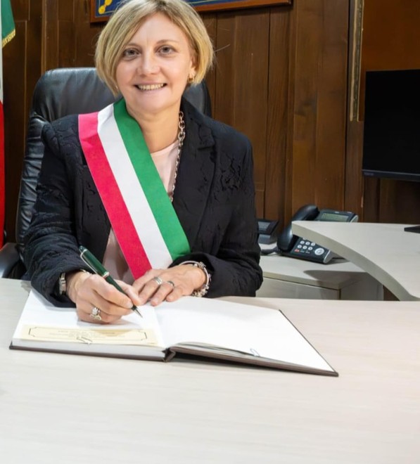 Donna sindaco con fascia tricolore che firma documenti